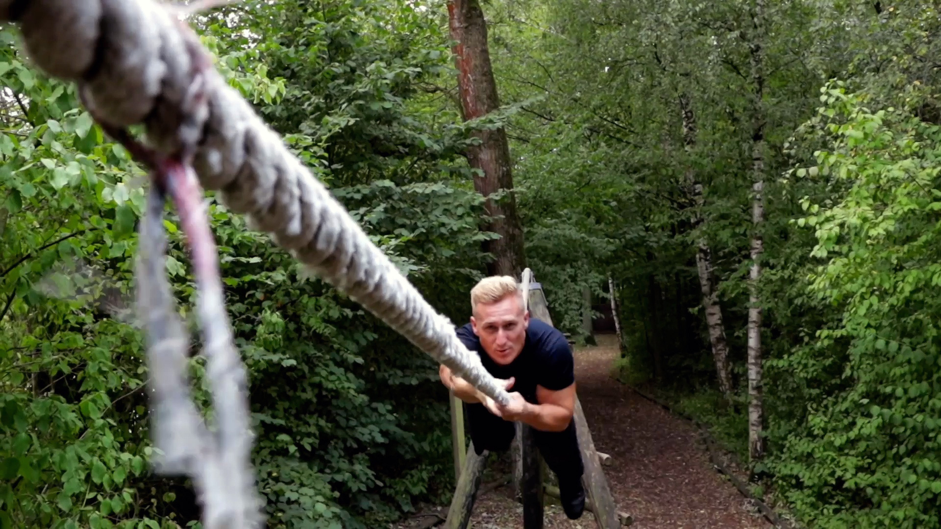 Junger Mann beim Training im Wald auf einem Seil hangelnd