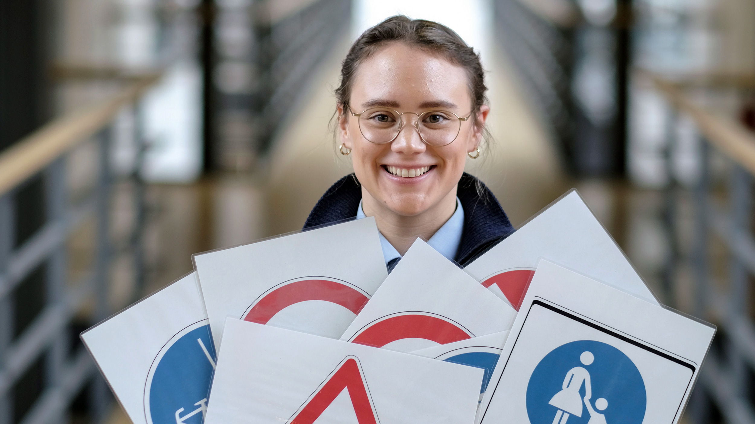 Junge Frau hält verschiedene Tafeln in den Händen, auf denen Verkehrsschilder abgebildet sind.