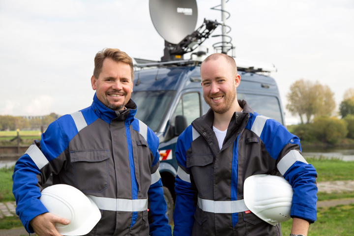 Zwei Männer in Berufsbekleidung vor einem größeren technischen Fahrzeug