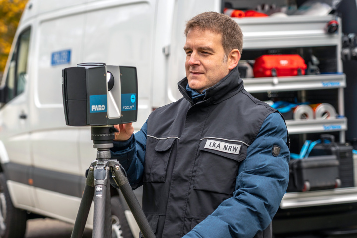 Ein Mann vom Landeskriminalamt steht mit einem Messgerät vor einem Fahrzeug das mit technischem Gerätschaften befüllt ist.