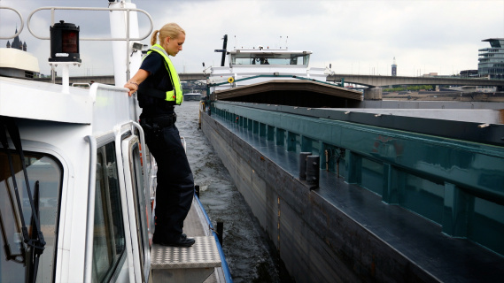 Policewoman Heller on the water police boat, in front of her a cargo ship, which she is about to board.